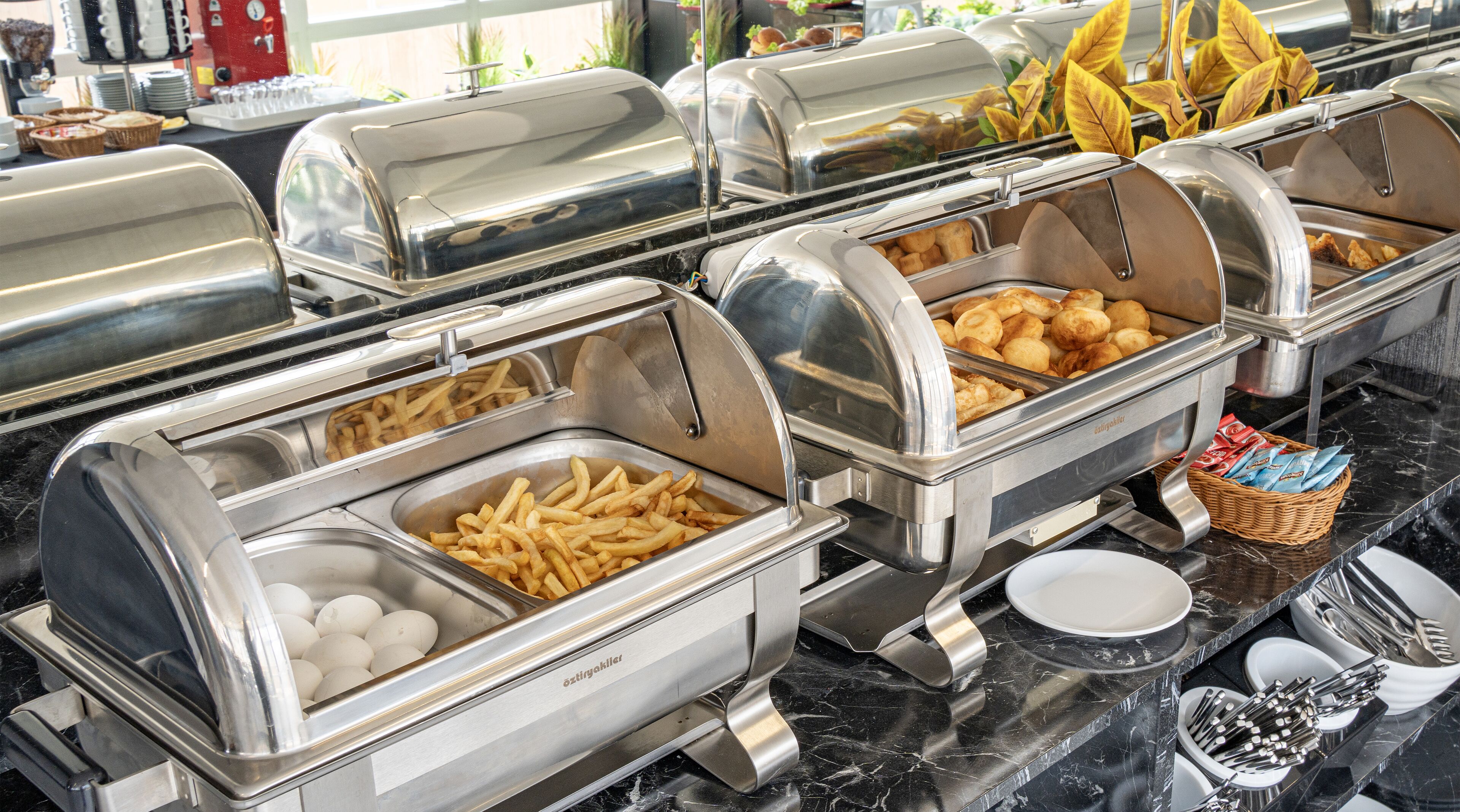 A buffet setup with various food items including French fries, eggs, and bread.