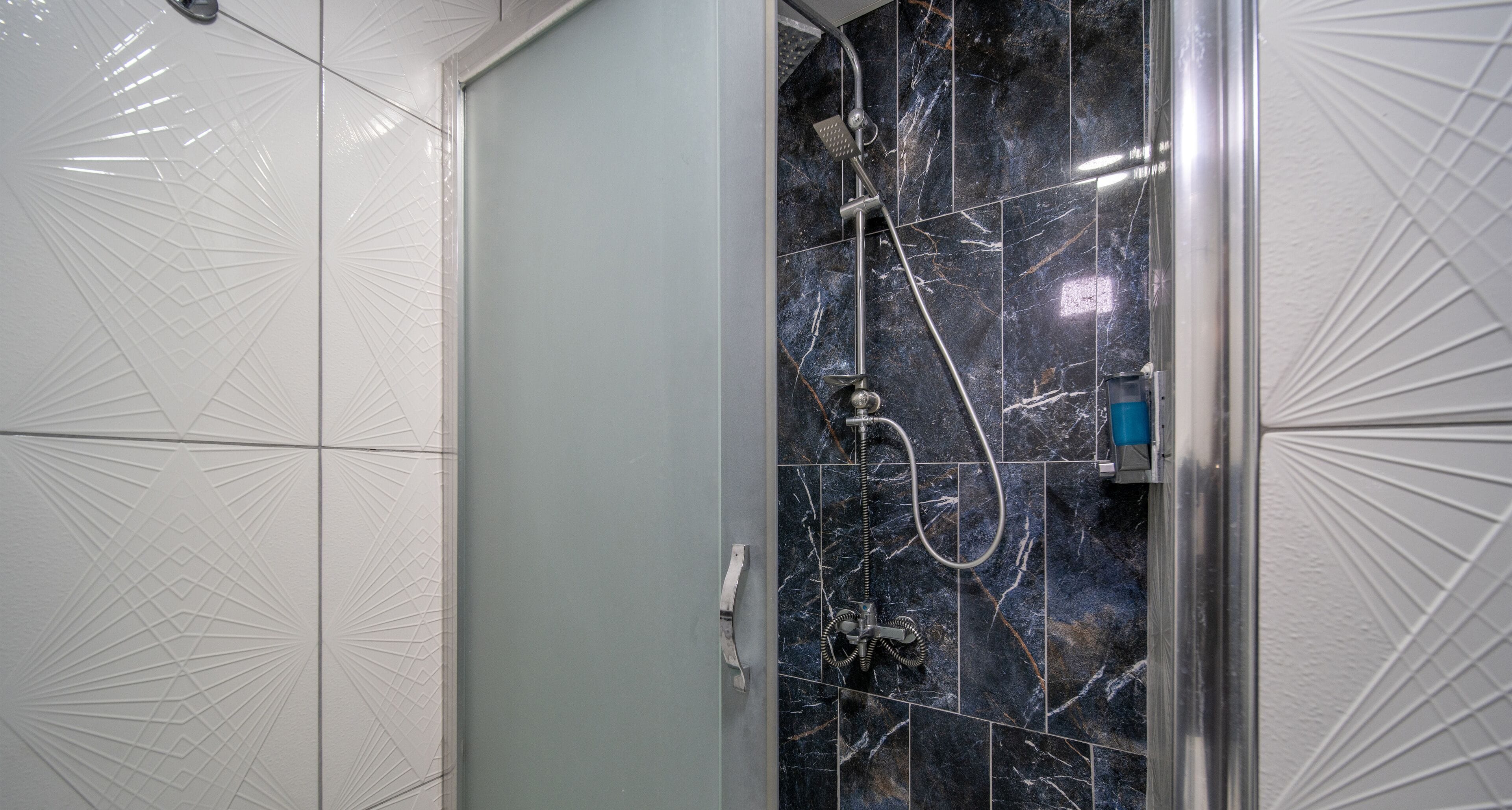 A bathroom with a shower area featuring a glass door, a handheld showerhead, and a handheld faucet.