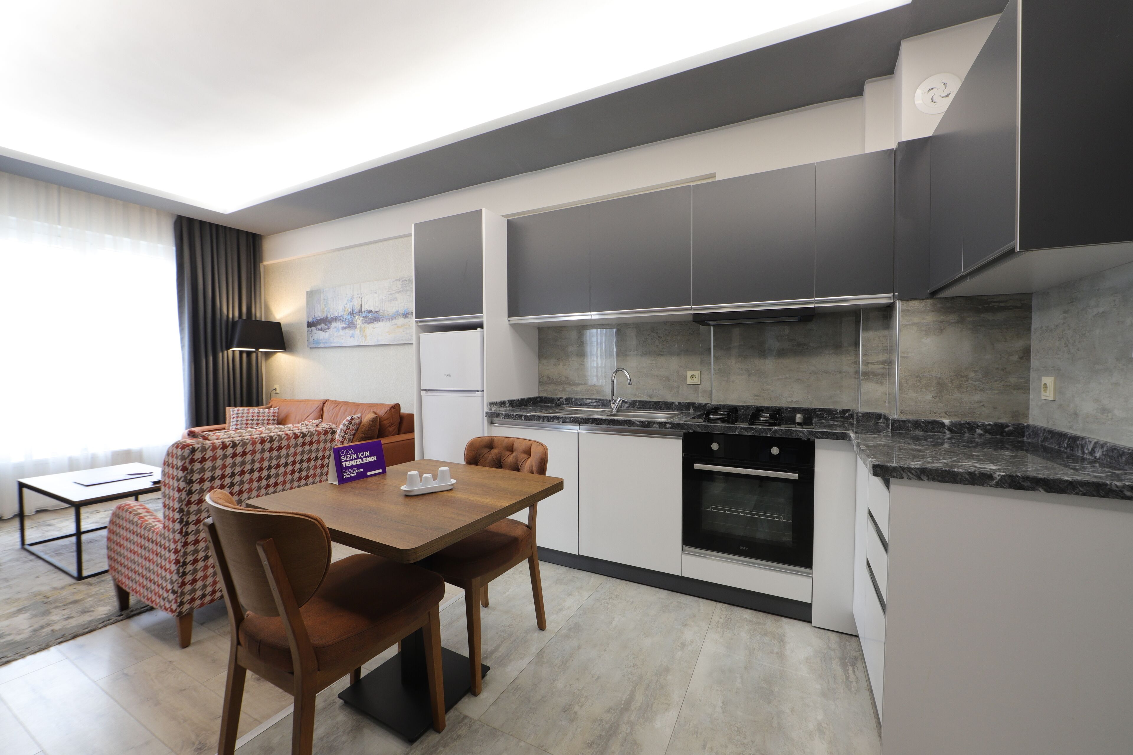 A modern kitchen with a dining area, featuring a marble countertop, built-in oven, and a sofa with a houndstooth pattern.
