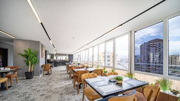A modern dining area with large windows, a bar, and a view of a cityscape.