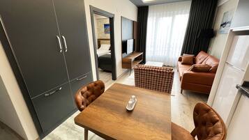 Une chambre d’hôtel moderne avec une table à manger en bois, des fauteuils en cuir marron, un canapé, une télévision et une armoire.