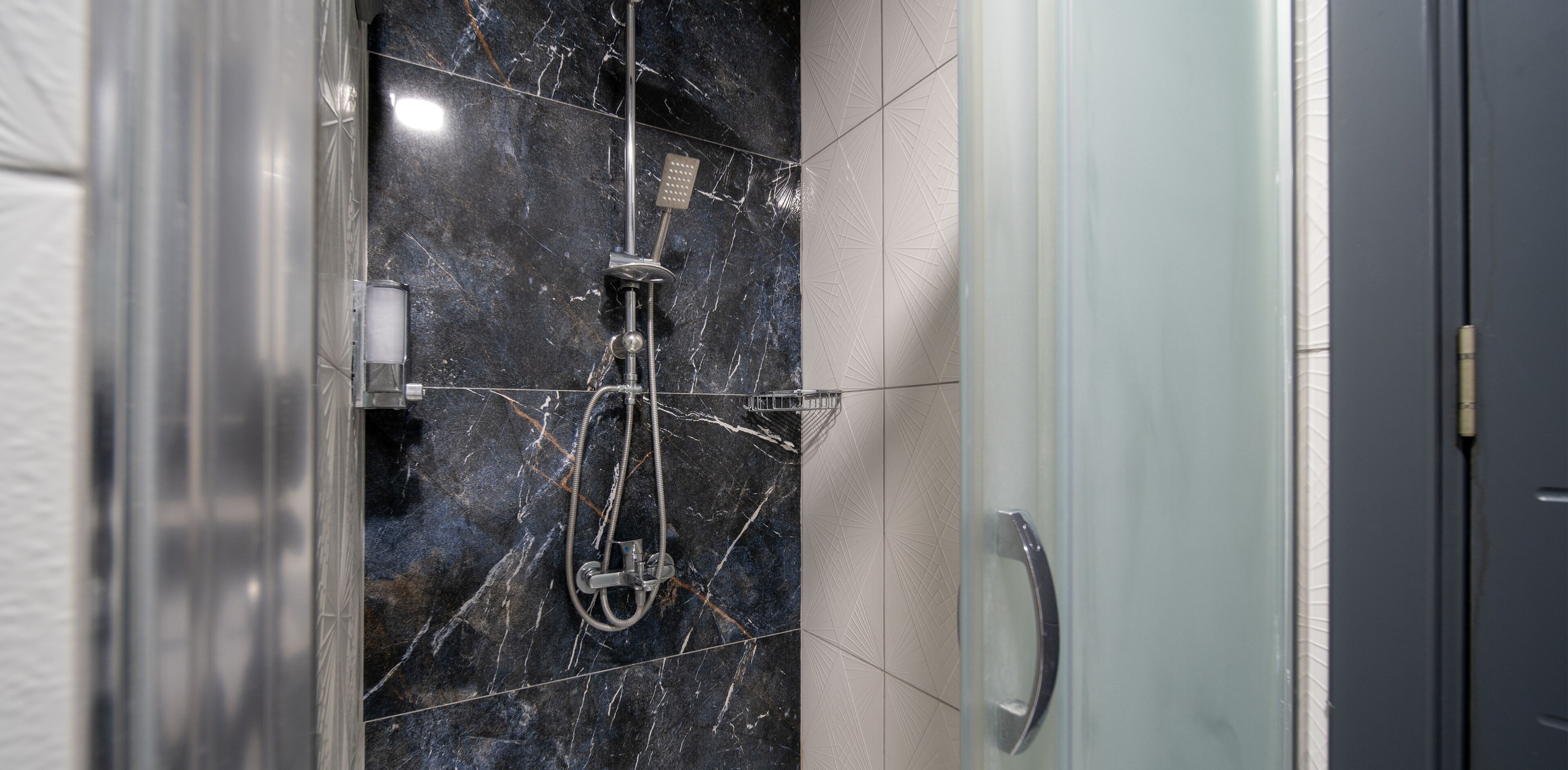 Un baño moderno con cabina de ducha de vidrio, ducha de mano y grifo empotrado.
