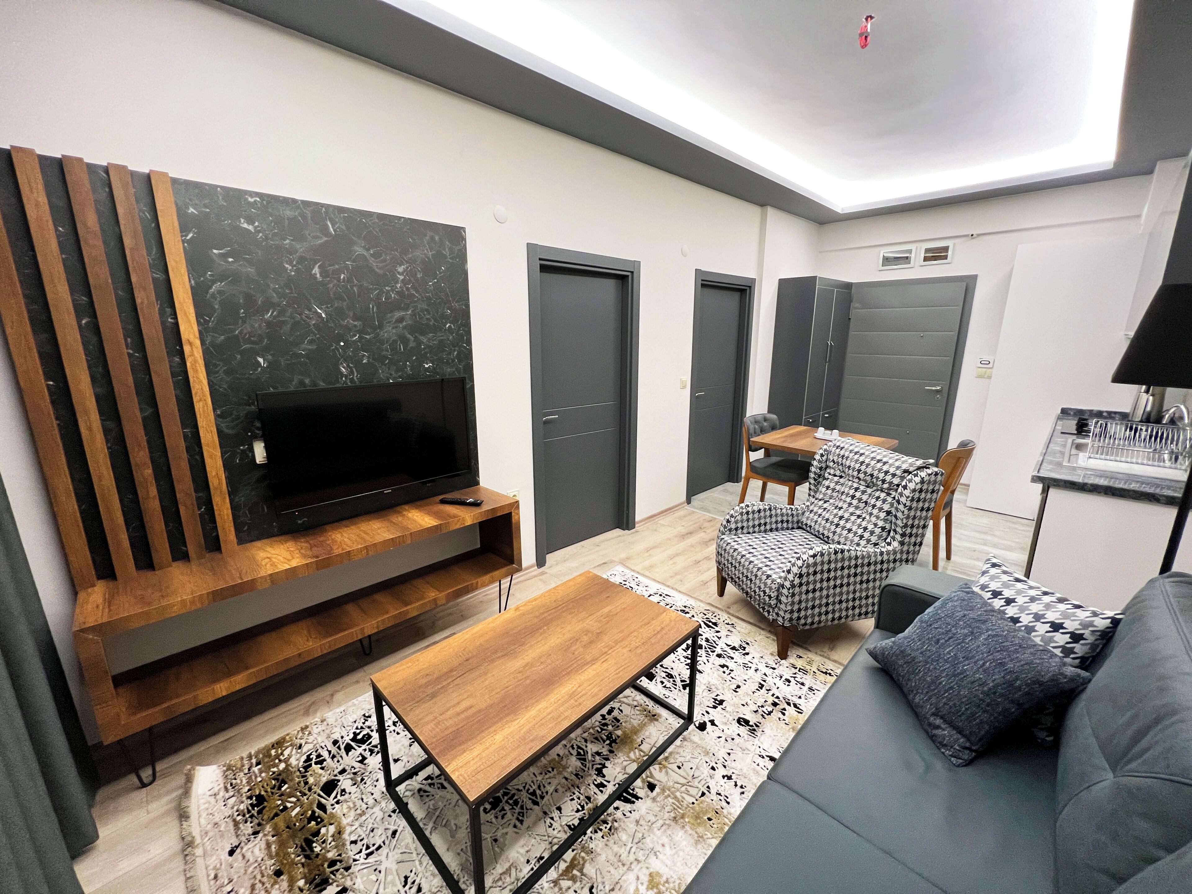 A modern living room with a flat-screen TV, wooden entertainment unit, sofa, and houndstooth patterned chair.