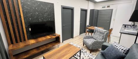 A modern living room with a flat-screen TV, wooden entertainment unit, sofa, and houndstooth patterned chair.