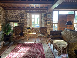 A cozy room with stone walls, a wooden ceiling, and a red patterned rug. There are two ornate chairs, a sofa, and a small table with a candelabra. - Elegant , historic country house ..ideal  to see D Day beaches &Mont St MIcheal (Saint-Denis-le-Gast)