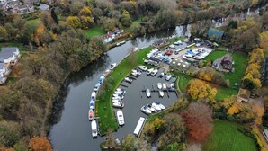 Luchtbeeld van een jachthaven aan de rivier, met aangemeerde boten, omgeven door herfstkleurige bomen en woongebouwen.