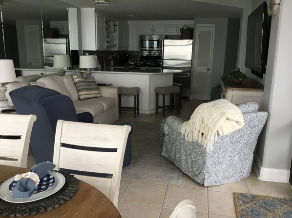 En moderne stue med en sofa, et spisebord med mad på, og et køkkenområde med hårde hvidevarer i baggrunden.