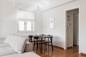 Ein modernes Wohnzimmer mit einer Couch, einem Esstisch mit Stühlen, einem Fenster mit Jalousien und einer Tür zu einem anderen Raum.