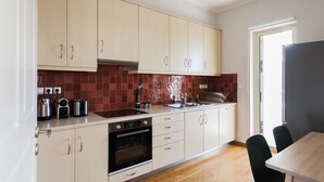 A modern kitchen with light-colored cabinets, a stainless steel sink, and a wooden dining table with black chairs. - Exquisite 2BR Apartment (Agia Paraskevi)