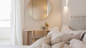 A bedroom with a bed, a desk, a chair, a round mirror, and a bedside lamp. - Exquisite 2BR Apartment (Agia Paraskevi)