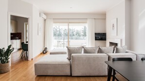 A modern living room with a sofa set, a dining area, and a kitchen visible through an open doorway. - Exquisite 2BR Apartment (Agia Paraskevi)