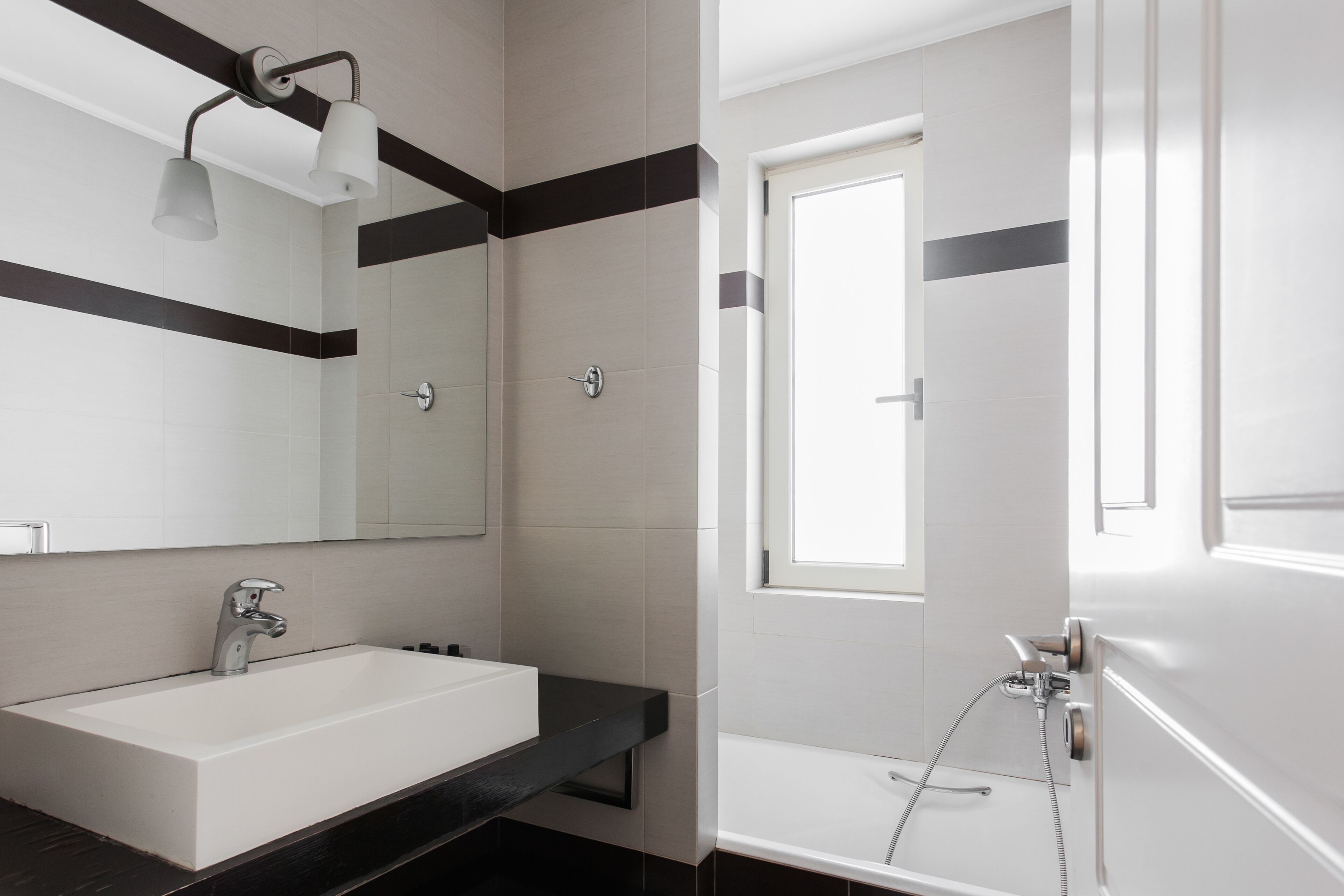 Un baño moderno con lavamanos blanco, encimera negra y un espejo grande.