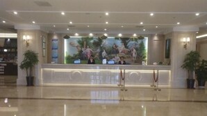A hotel reception area with a large mural, reception desk, and two potted plants. - Vienna International Hotel Kunshan Lujia Shentongyu Subway Station (Kunshan)