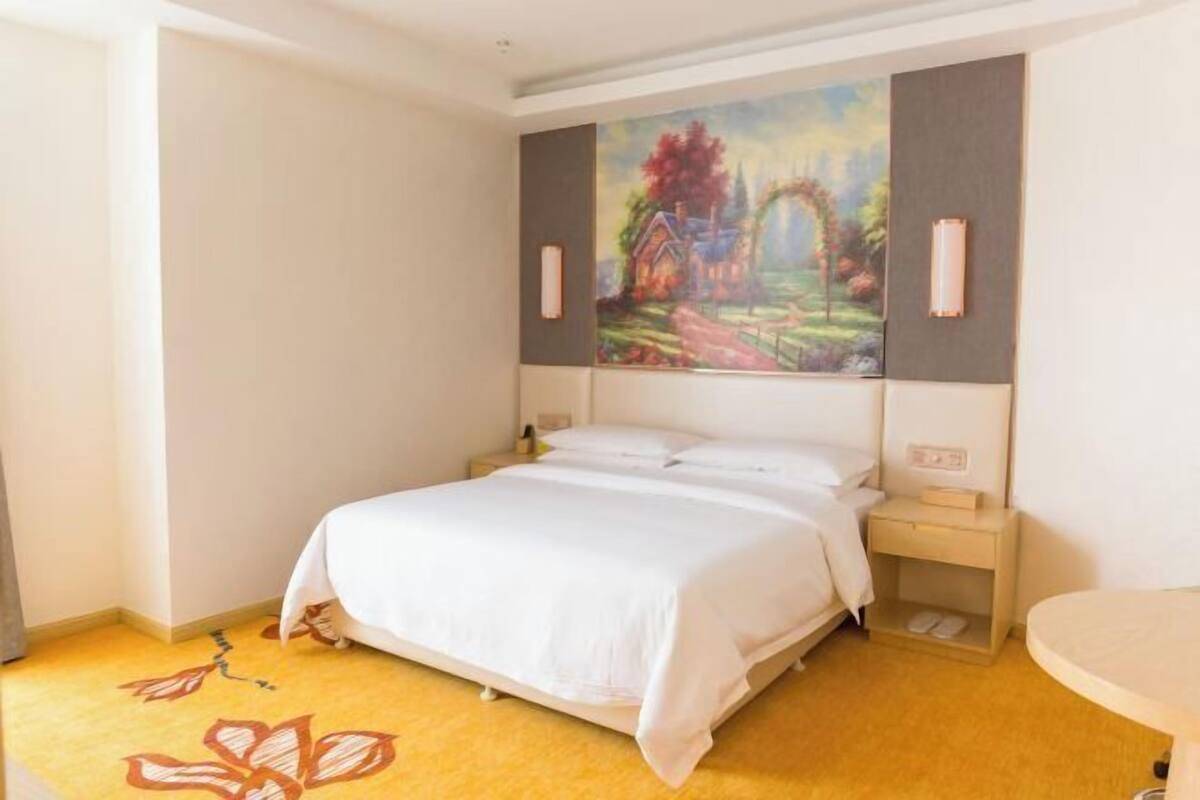 Una camera d'albergo con un letto, un comodino, un quadro appeso al muro e un piccolo tavolo.