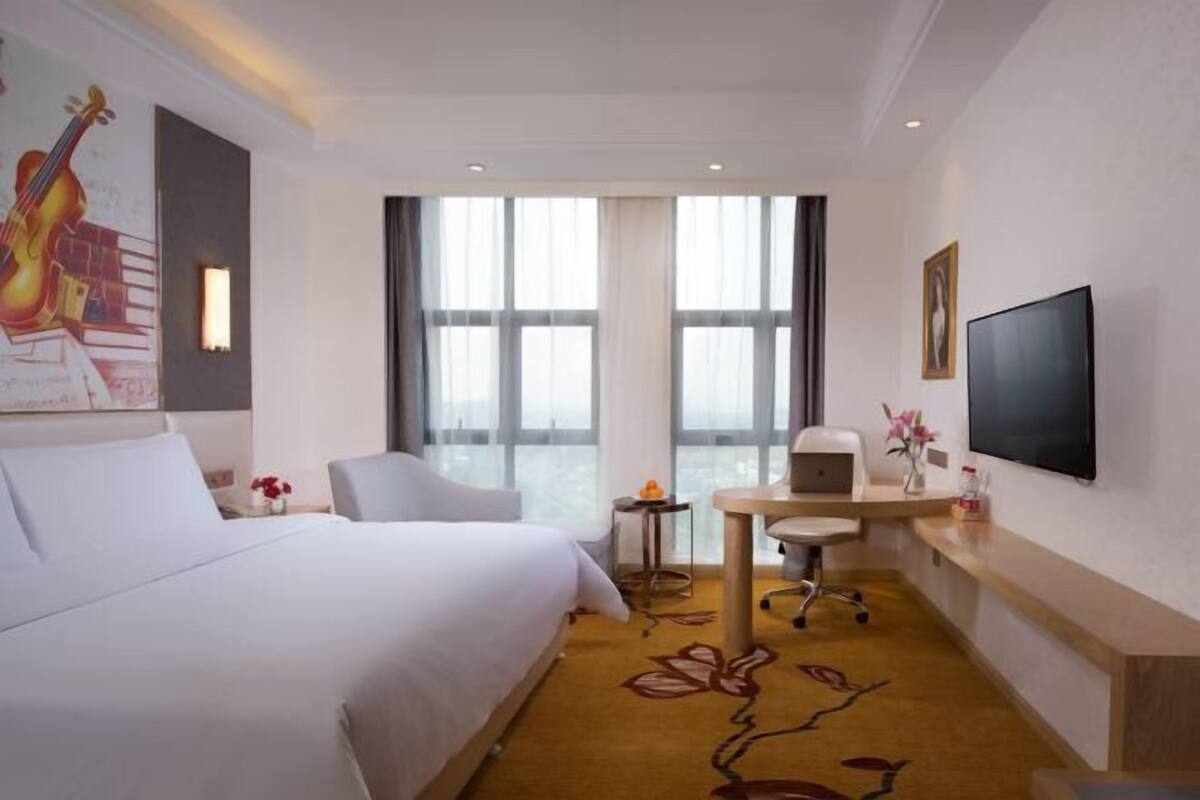Camera d'albergo con un letto, una scrivania, una sedia, una TV e ampie finestre.