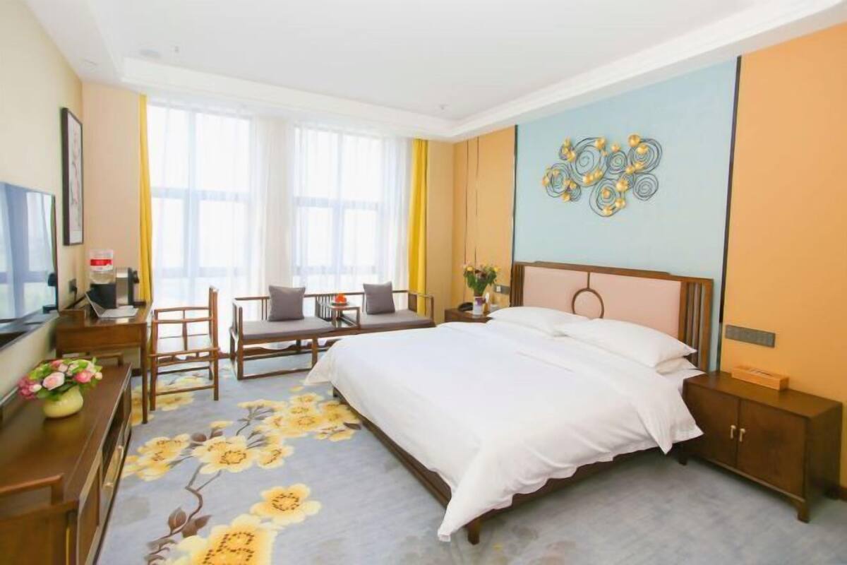 Camera d'albergo con un letto, una scrivania con sedia, una televisione e una finestra con tende.