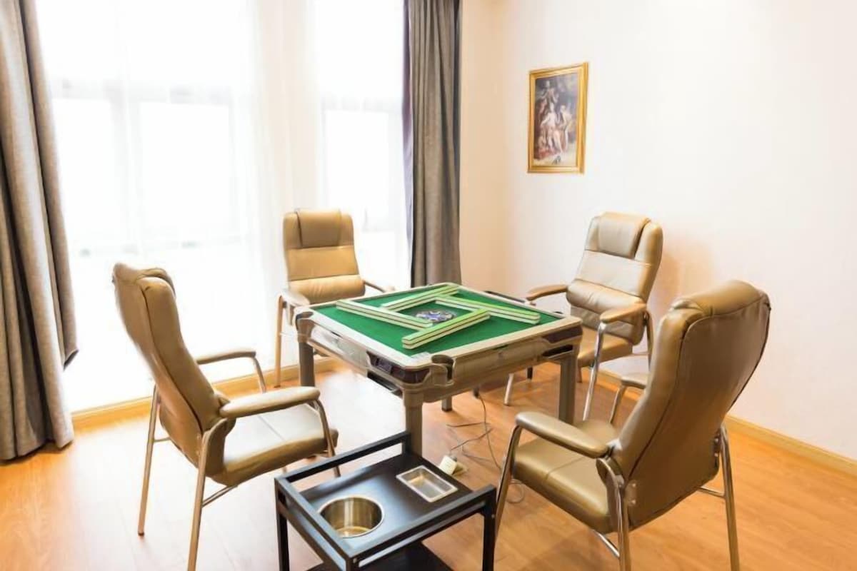 A room with a green pool table, four beige chairs, and a small table with a slot.