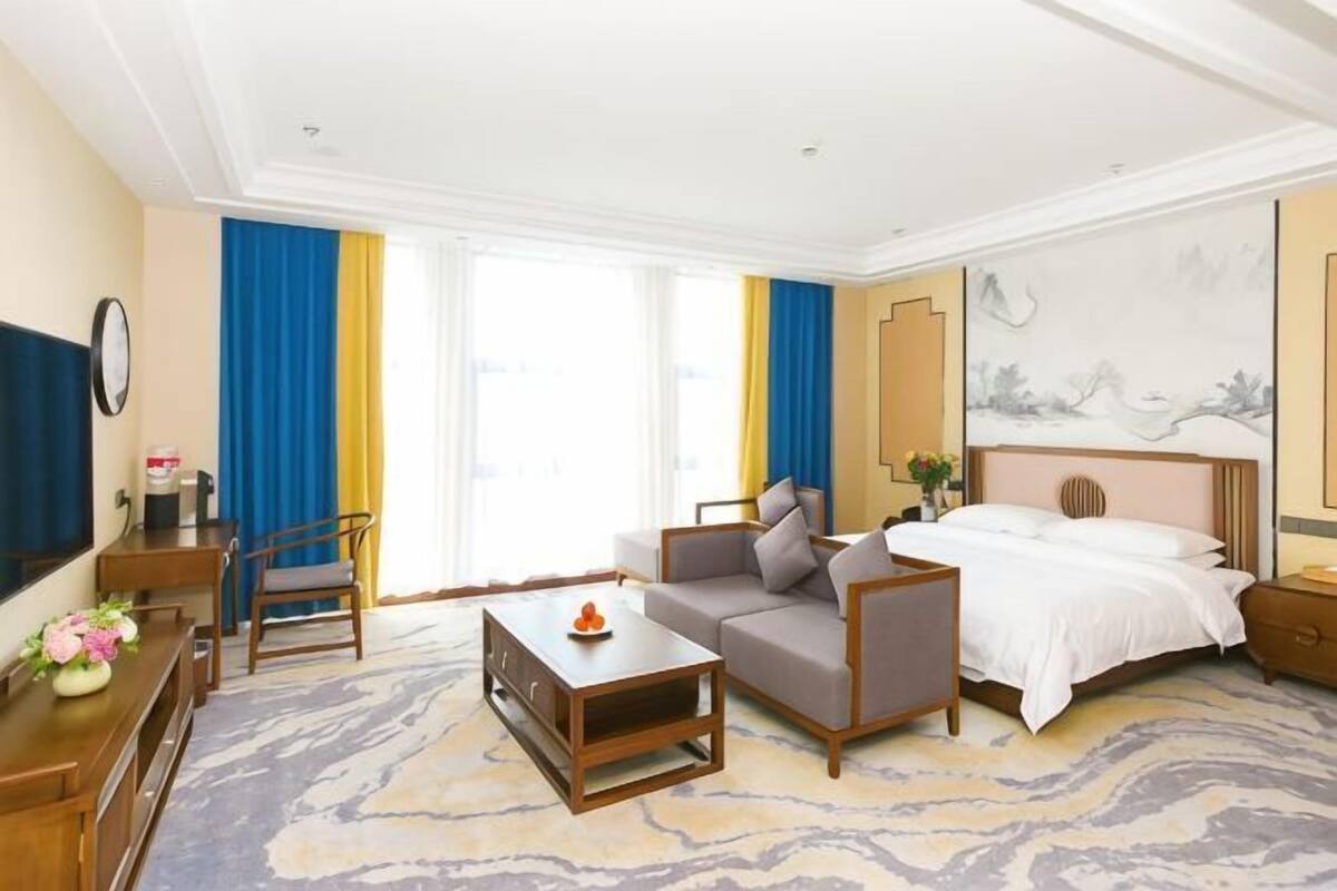 Una camera d'albergo con un letto, un divano, un tavolino, una televisione e una scrivania con una sedia.