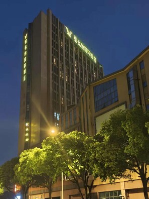 A high-rise building with illuminated signage, surrounded by trees and streetlights. - Vienna International Hotel Kunshan Lujia Shentongyu Subway Station (Kunshan)