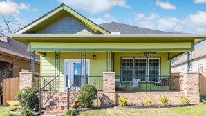 Uma casa de dois andares com fachada verde, varanda frontal com corrimão e fundação de tijolos.