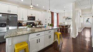 Uma cozinha moderna com armários brancos, bancadas de granito, eletrodomésticos de aço inoxidável e banquetas amarelas.