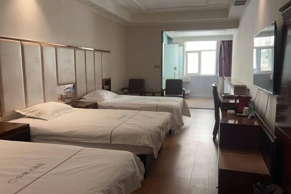 A hotel room with two beds, a desk, a chair, and a television.