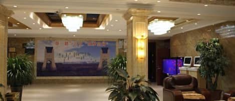 A hotel lobby with a large mural, comfortable seating, and a reception area with monitors.