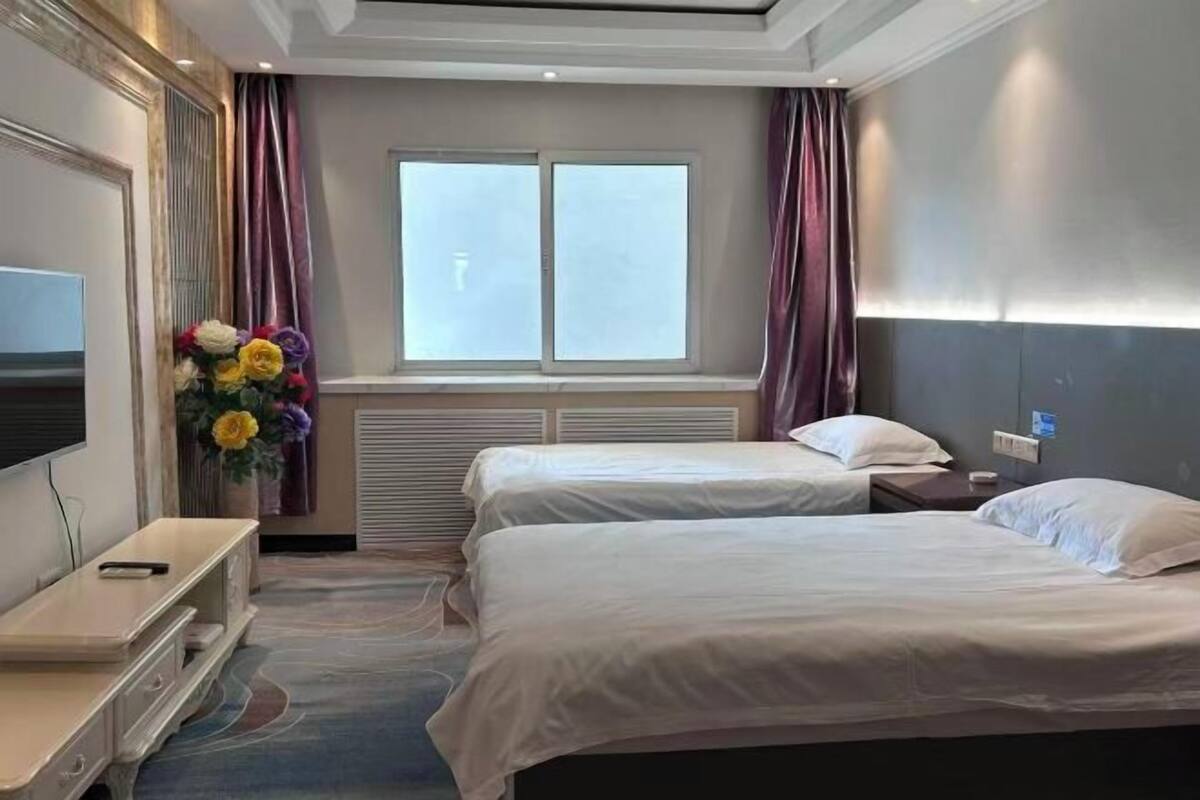 A hotel room with two beds, a TV, a desk, and a window with curtains.