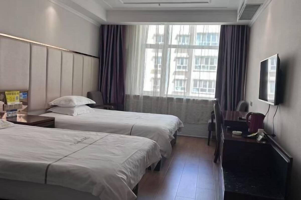 A hotel room with two beds, a desk, a chair, a TV, and a window with curtains.