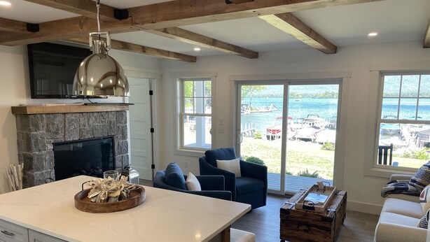 A modern kitchen with a stone fireplace, a large island, and a view of the sea through the sliding glass doors. - Direct Waterfront Rental  (Lake George)