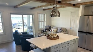A modern kitchen with a large island, stainless steel appliances, and a view of boats through the glass door. - Direct Waterfront Rental  (Lake George)