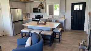 A modern kitchen with stainless steel appliances, a central island with seating, and a black door. - Direct Waterfront Rental  (Lake George)