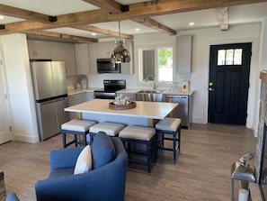 A modern kitchen with stainless steel appliances, a central island with seating, and a black door. - Direct Waterfront Rental  (Lake George)