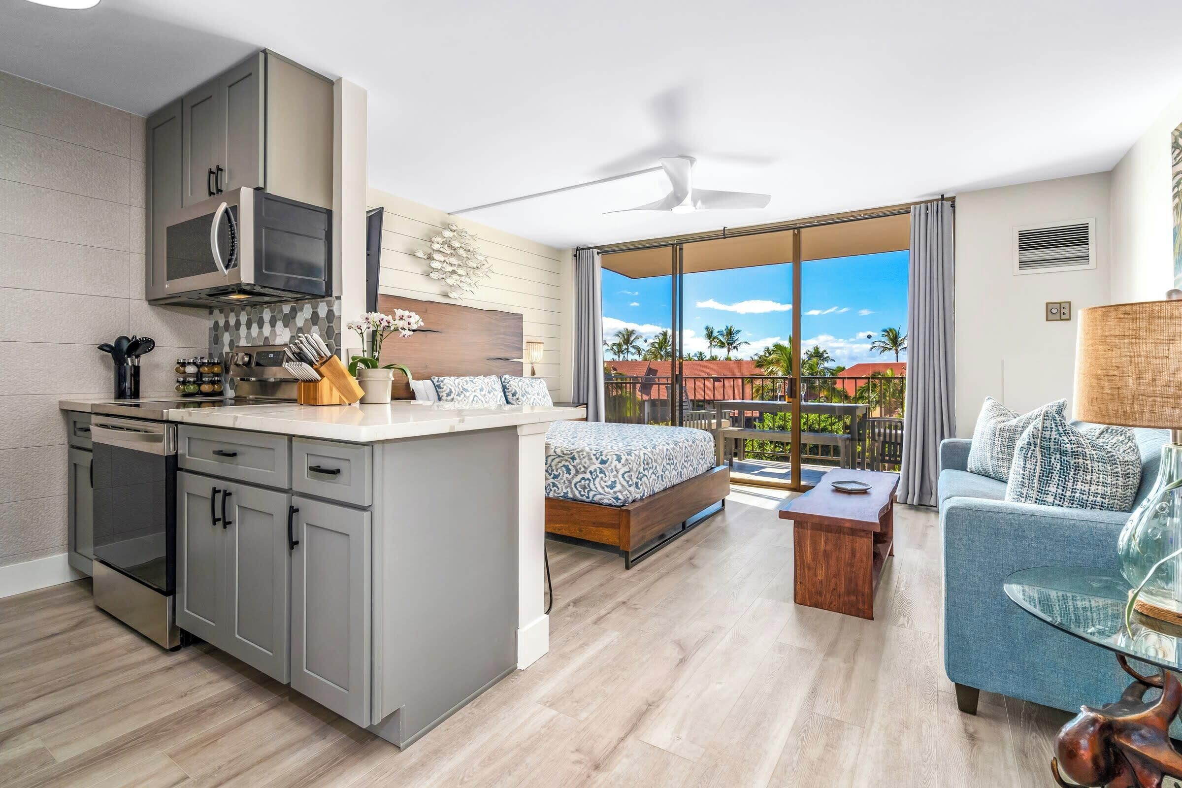 A modern hotel room with a kitchen, a balcony with a view, a bed, and a seating area.