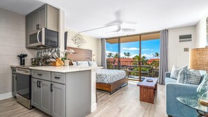 Moderni hotellihuone, jossa on keittiö, parveke, jolta on näkymä, sänky ja oleskelualue.
