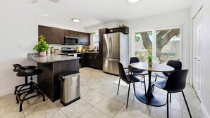 A modern kitchen with dark cabinets, stainless steel appliances, a central island with bar stools, and a dining area with chairs.