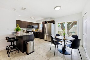 A modern kitchen with dark cabinets, stainless steel appliances, a central island with bar stools, and a dining area with chairs.