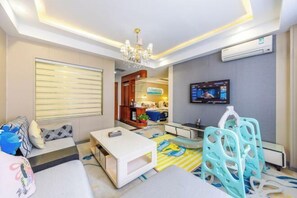 A modern hotel room with a sofa, a small table, a TV, and a kitchenette area.