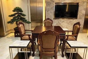 A conference room with a large table, six chairs, a potted bonsai tree, a flat-screen TV mounted on the wall, and a marble floor.