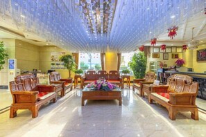 Um saguão de hotel com área de estar central, balcão de recepção e um lustre.