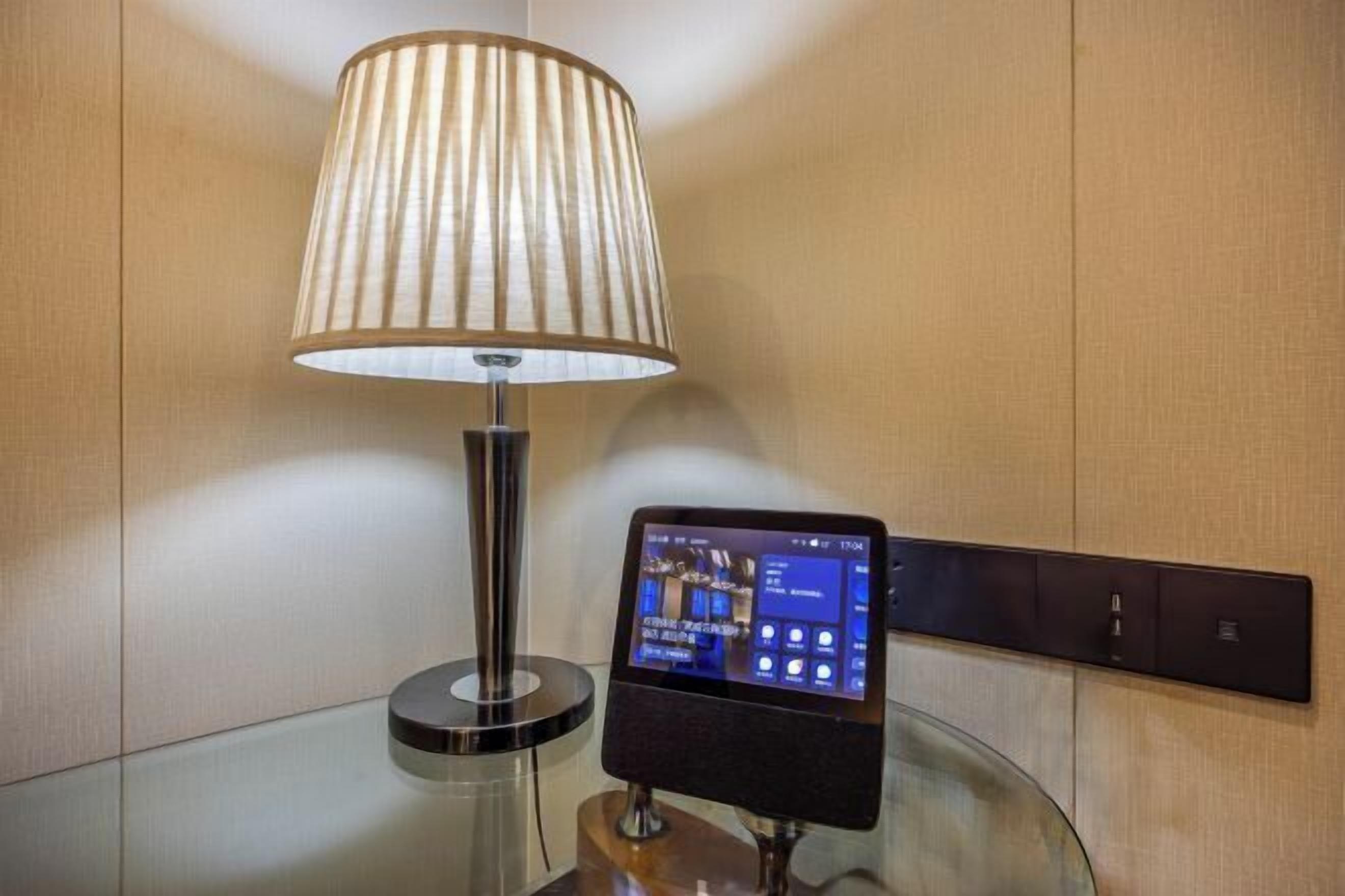 Une lampe moderne dotée d’un écran numérique, posée sur une table en verre, avec un panneau fixé au mur et un mur à texture.