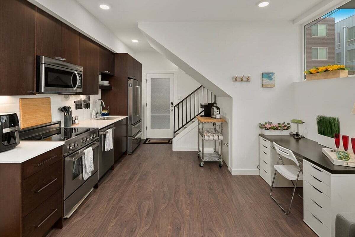 A modern kitchen with dark wooden cabinets, stainless steel appliances, and a white countertop.