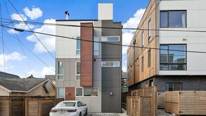 A modern two-story residential building with a car parked in the driveway. - Perch - Centro Guesthouse F: Walkable, Parking, Rooftop Deck & Pet Friendly (Seattle)