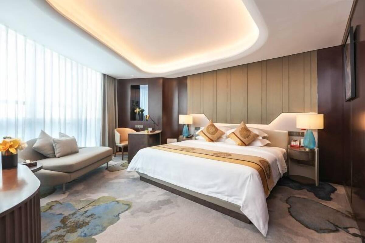 Een moderne hotelkamer met een groot bed, twee bedlampen, een sofa en een bureau met een lamp.