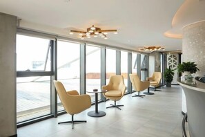 Un moderno vestíbulo de hotel con amplios ventanales, sillas contemporáneas y una lámpara central.