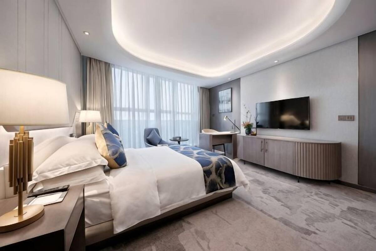 Een moderne hotelkamer met een groot bed, nachtkastje, lamp, bureau, stoel en een flatscreen televisie aan de muur.