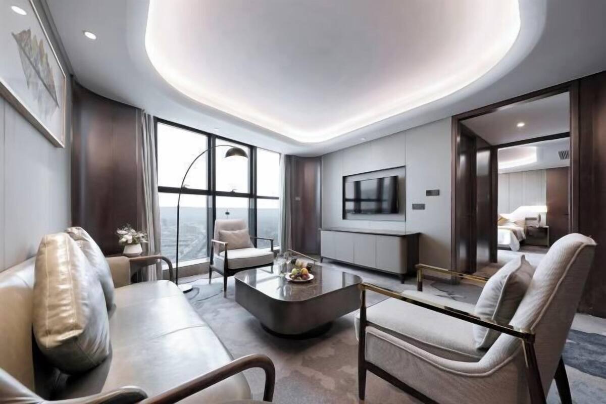 Een moderne woonkamer met een gebogen plafond, een flatscreen televisie aan de muur en een groot raam met uitzicht op de stad.