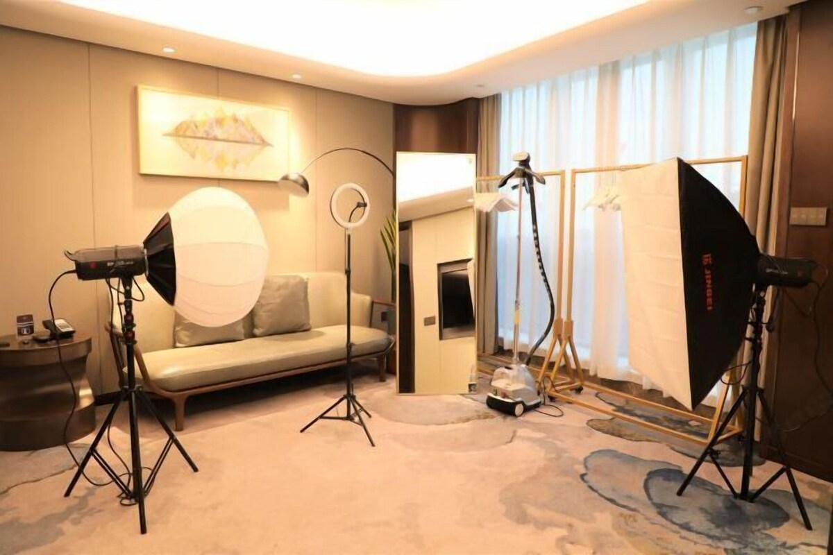 Ein Hotelzimmer mit einer Couch, einem großen Fenster mit Vorhängen und professioneller Fotoausrüstung.