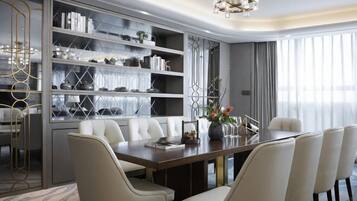 A modern dining area with a long table, white upholstered chairs, and a built-in bookshelf with decorative items.