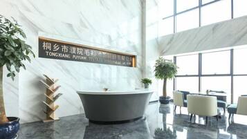 A modern interior with a marble reception desk, a large bathtub, and a seating area with chairs and tables.